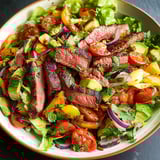 Un piatto di steak alla griglia su verdure fresche con pomodorini.